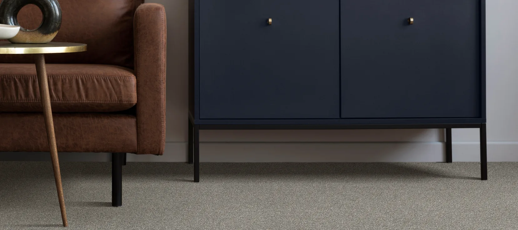 A modern living room with Engineered Floors carpet, featuring a brown leather couch, a small round table, and a navy cabinet.
