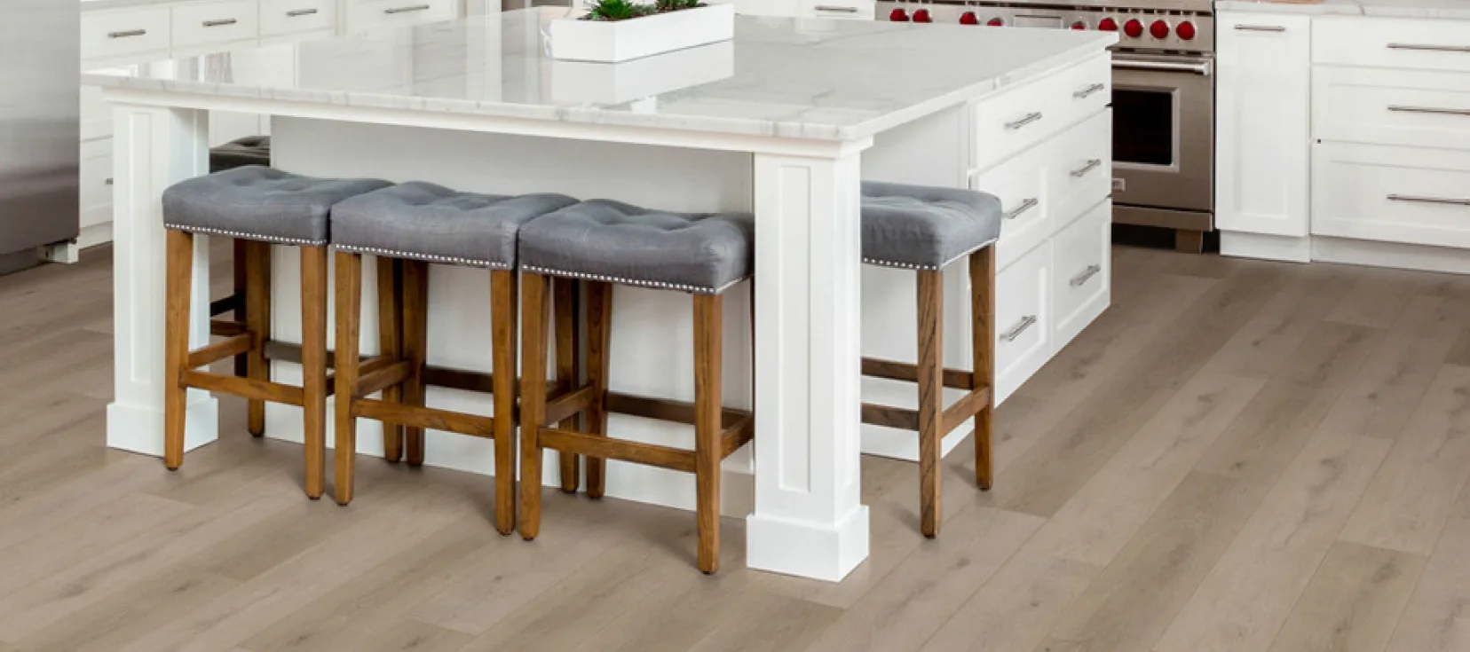 Modern kitchen with light wood plank flooring and a white island with gray cushioned stools.
