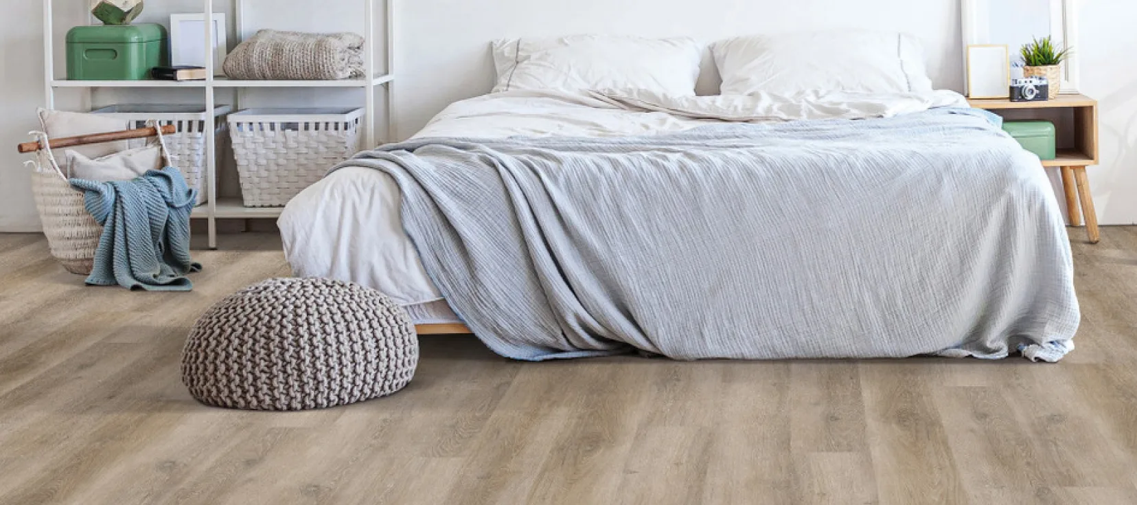 Cozy bedroom with light wood flooring and a neatly made bed with a light gray blanket.